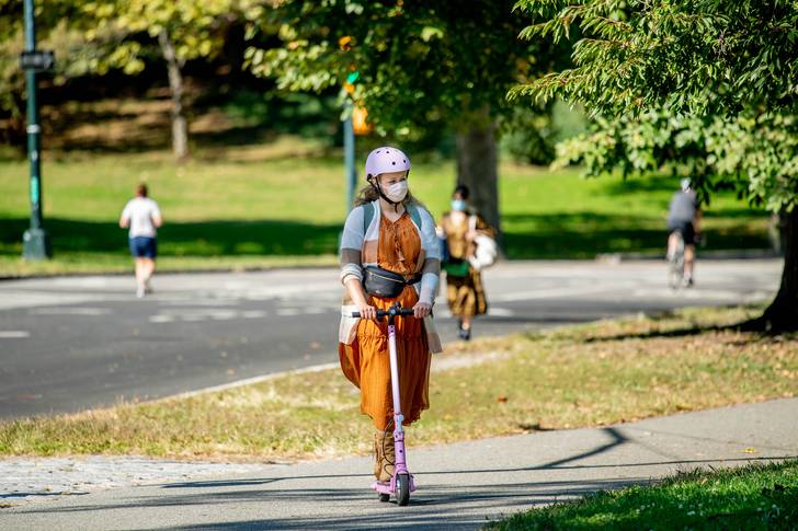 A woman wearing a helmet and face mask on a scooter on a path
